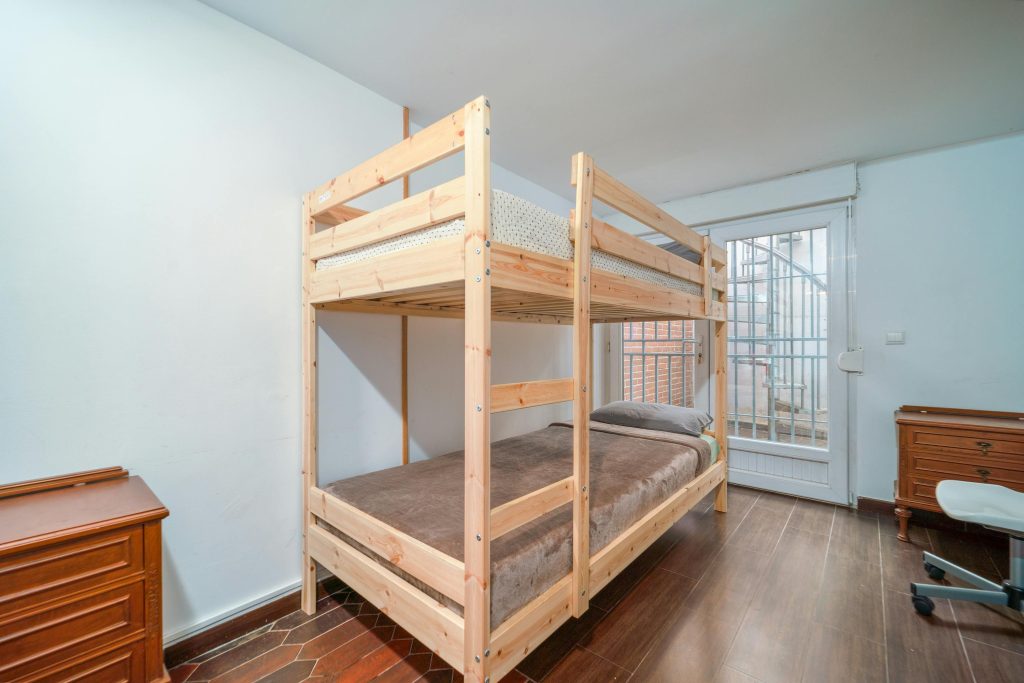 pexels-photo-12870114-12870114 Neat bedroom with a wooden bunk bed and minimalist decor, featuring natural lighting.